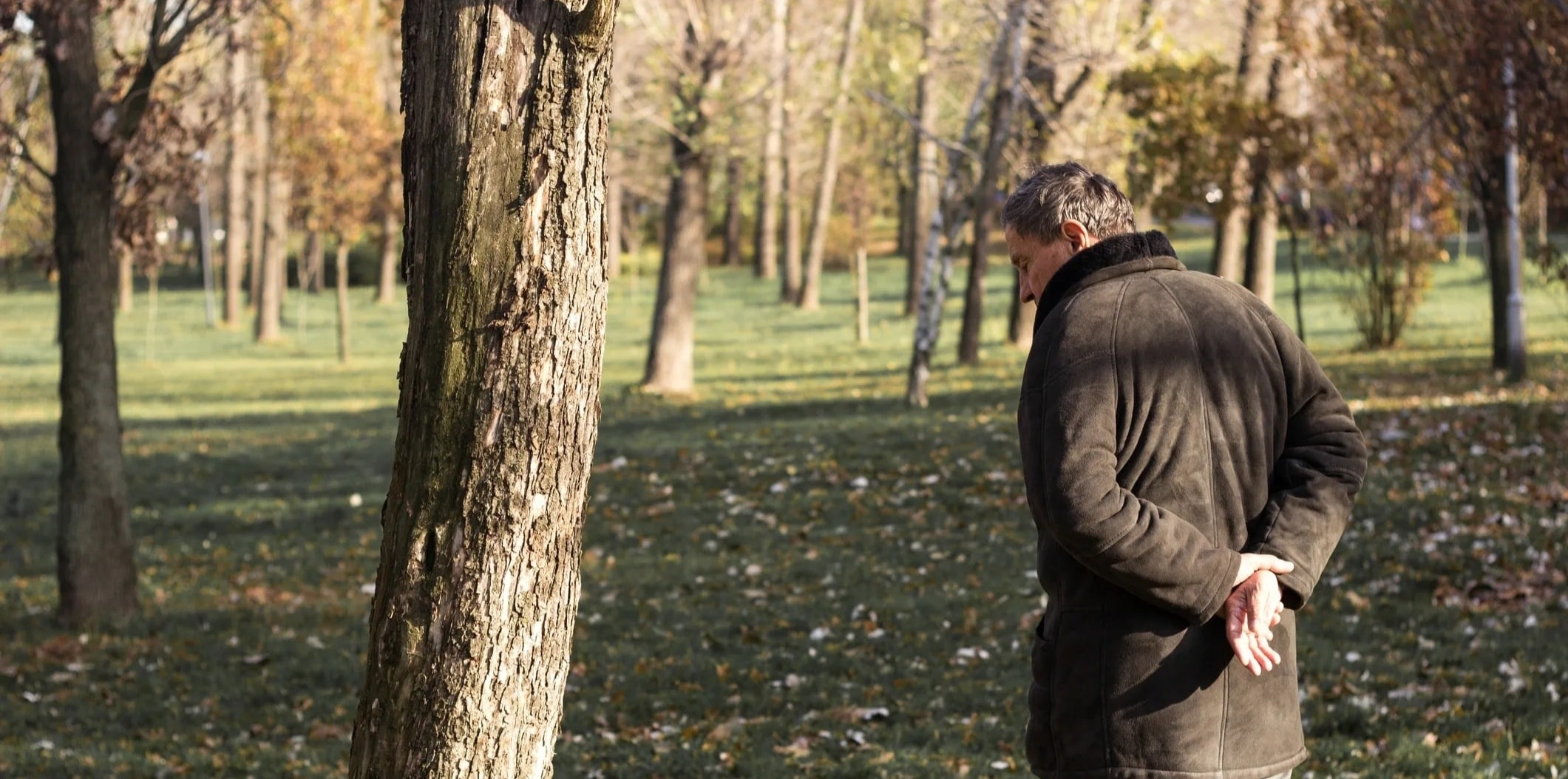A man in his 60s walking pensively through a park, processing grief in nature